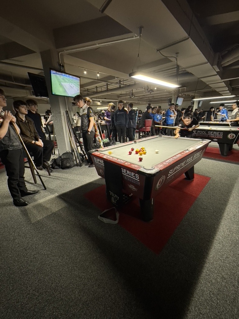A player down on a shot at a Supreme Pool Series table while spectators watch.